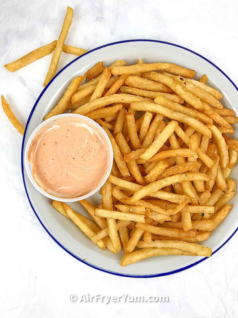 A grey plate with a blue rim that has French fries and a bowl of an orangish dipping sauce