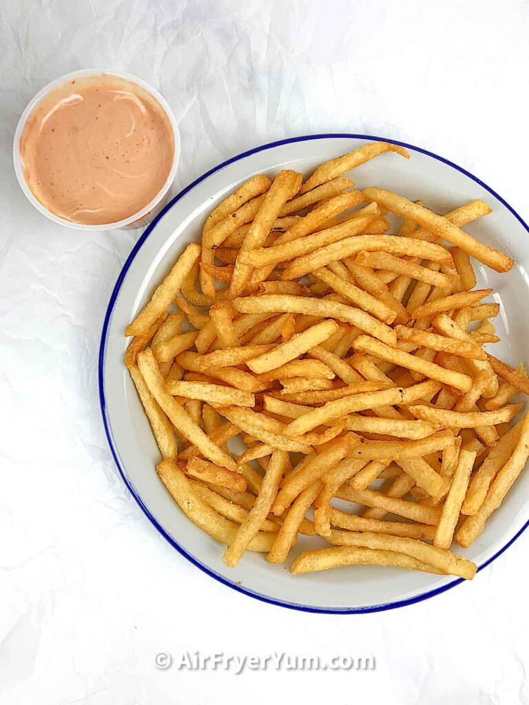 A grey plate of fries with a bowl dipping sauce on the top left corner