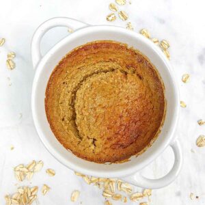 baked oats in a white ramekin with oat pieces all around the white table
