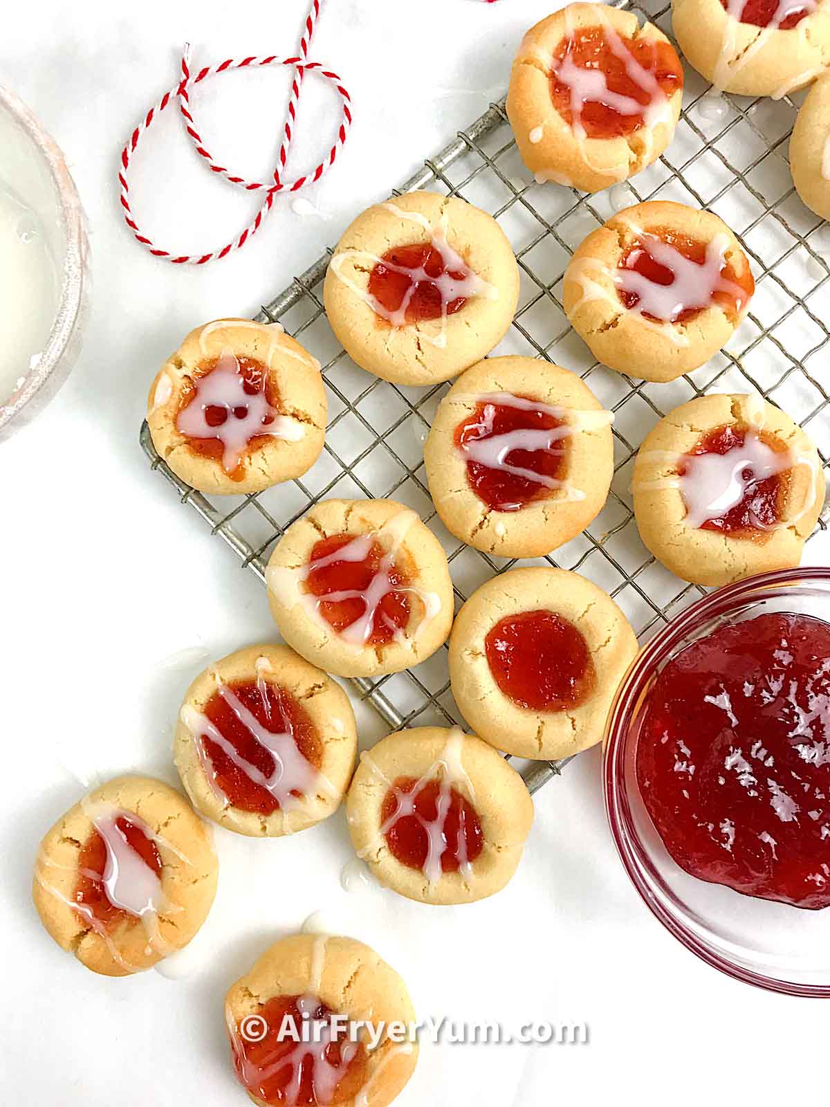 Jam filled cookies on a baking rack with a bowl of jam on the side
