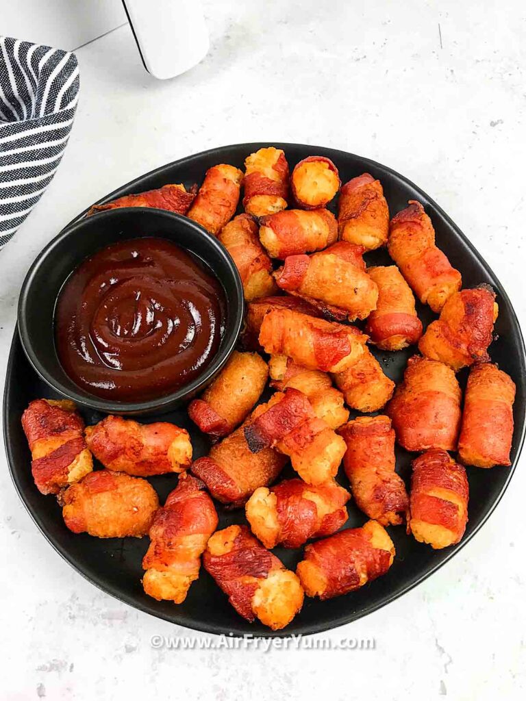 A back plate of wrapped tater tots with a black dipping bowl of bbq sauce