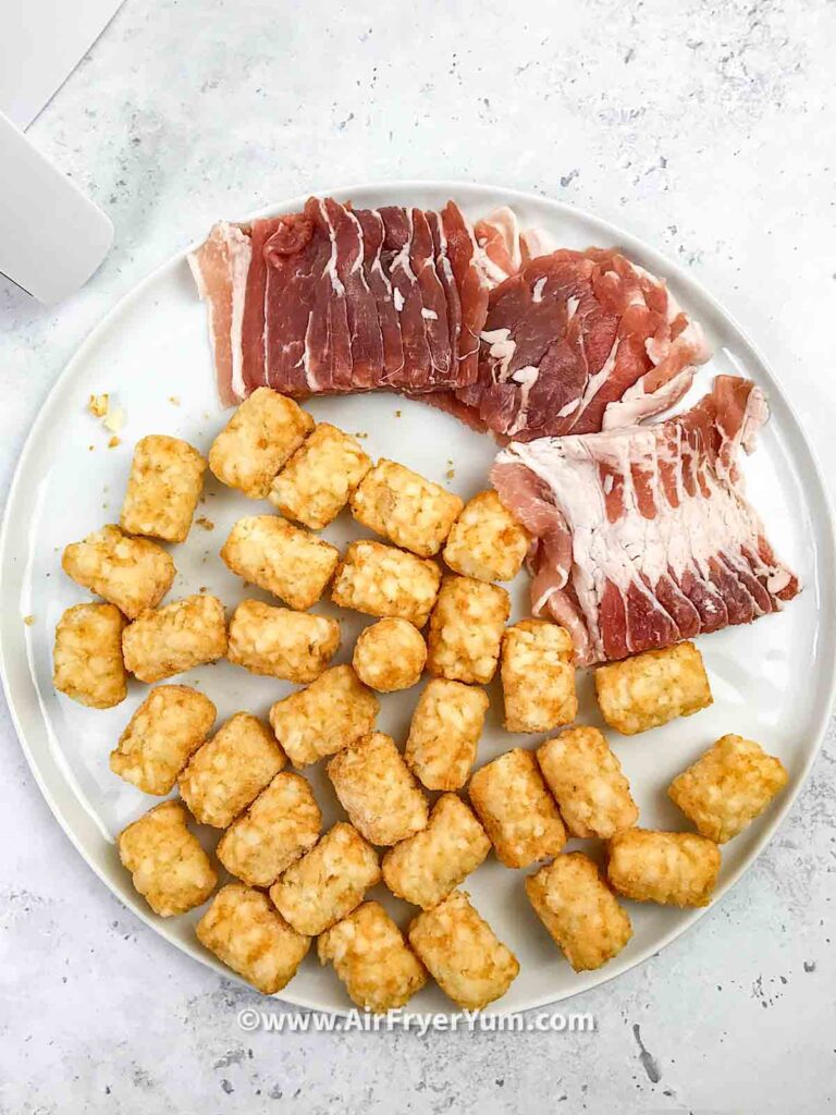Some frozen tater tots and slices of uncooked bacon on a white round plate on a white back ground 