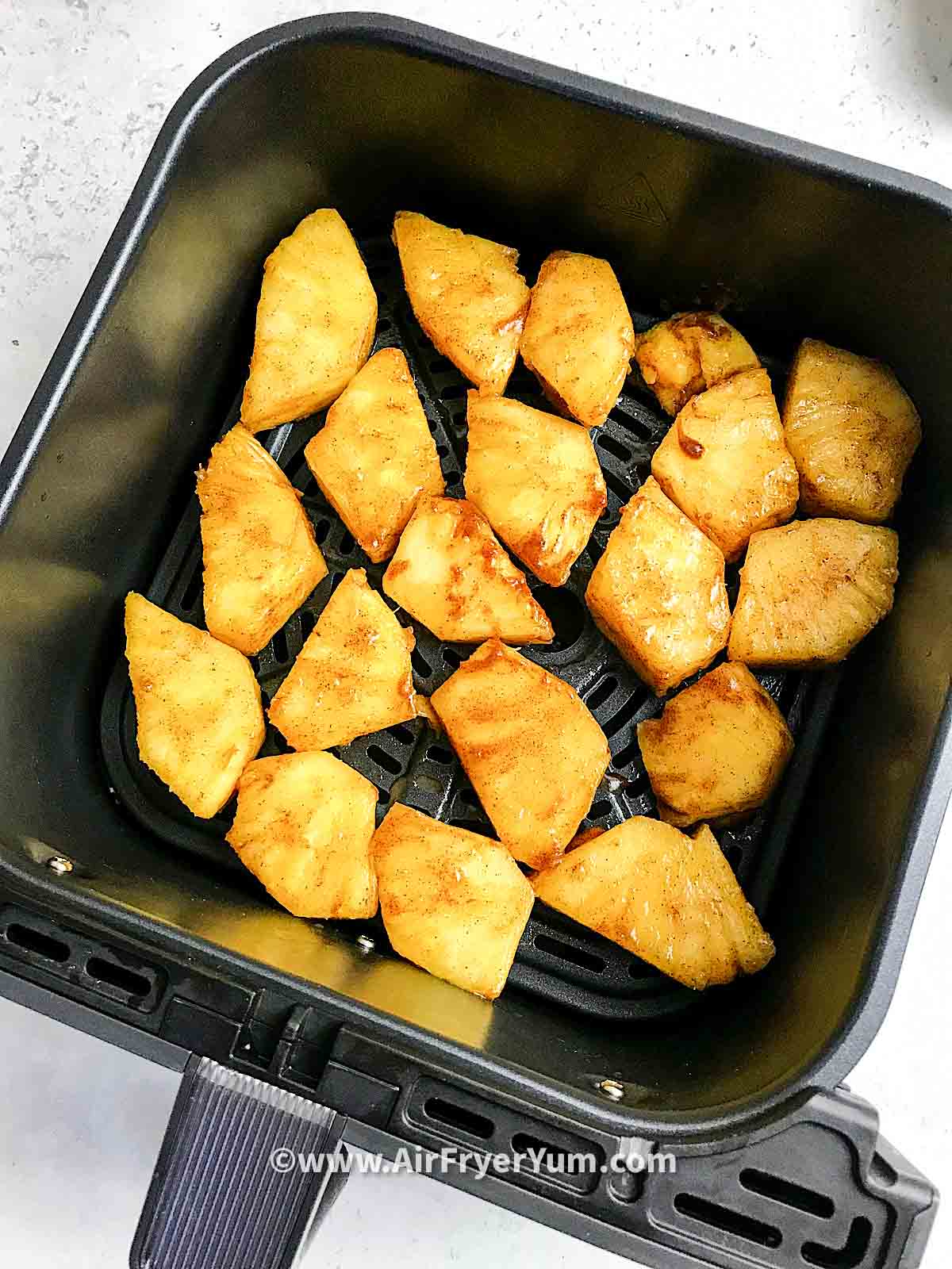 Fresh pineapple chunks glazed with cinnamon and brown sugar in a black air fryer basket.